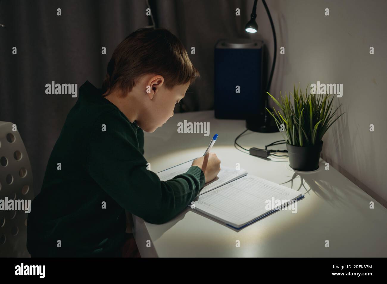 garçon caucasien faisant ses devoirs à la maison dans une pièce sombre à la lumière de la lampe. Image avec mise au point sélective Banque D'Images
