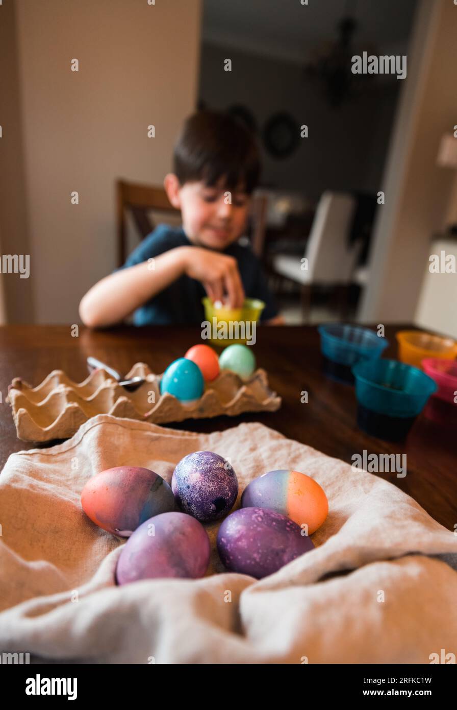 Pile d'oeufs de pâques colorés avec garçon mourant un oeuf en arrière-plan. Banque D'Images