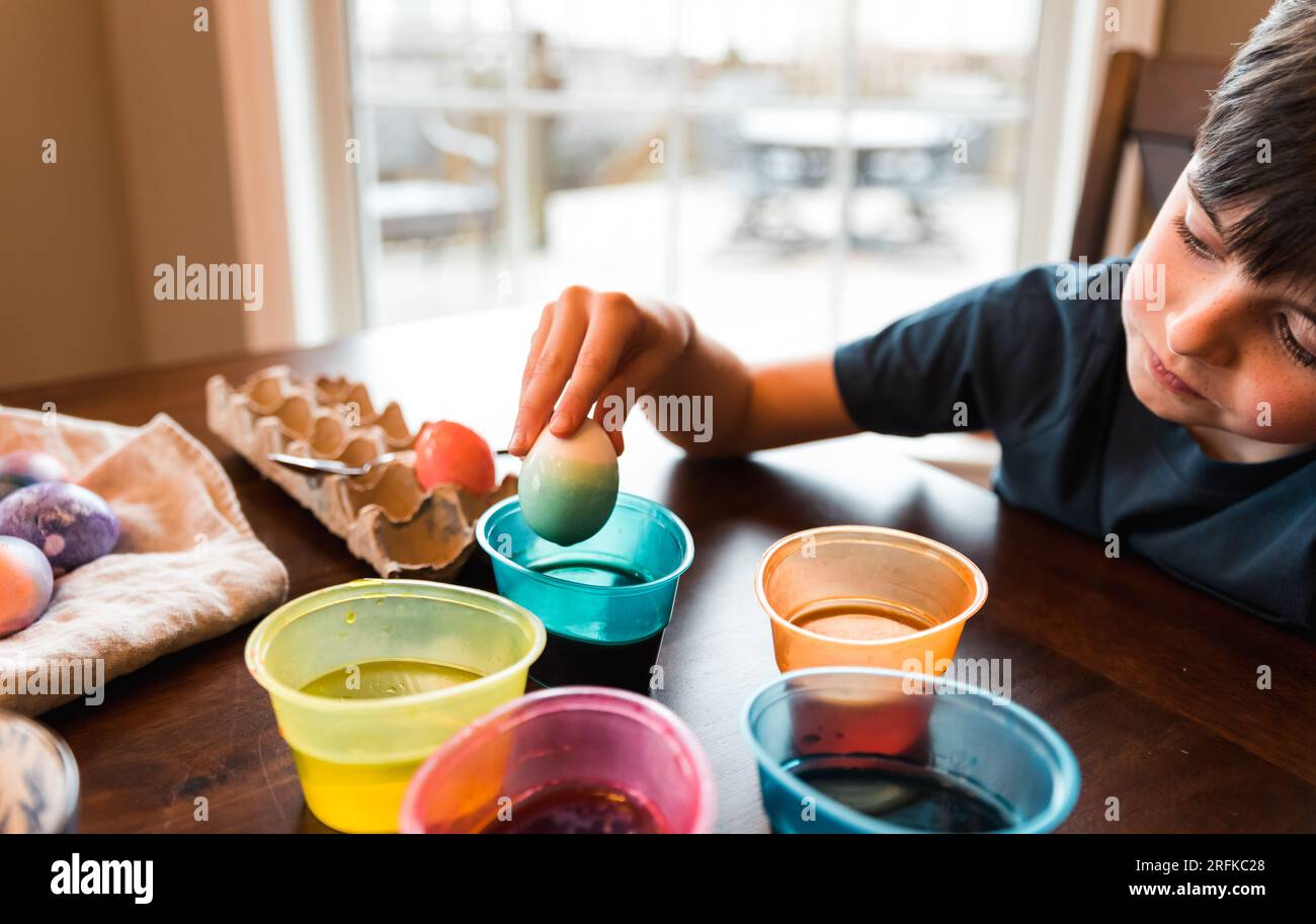 Garçon trempant un œuf dans un récipient de colorant pour le colorer pour pâques. Banque D'Images