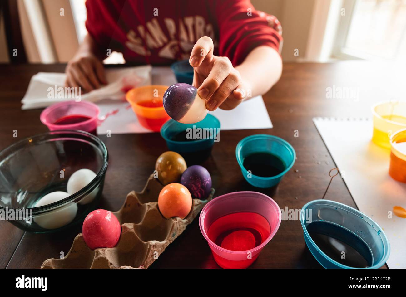Récolte de main tenant l'oeuf de pâques coloré avec des récipients de teinture à l'arrière. Banque D'Images