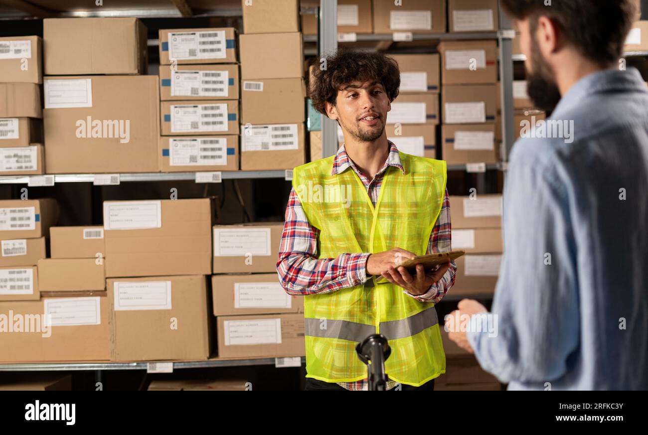 Les employés des magasins de vente au détail font la gestion des stocks. Gestionnaire d'entrepôt de service postal tenant la tablette numérique parlant avec le client Banque D'Images