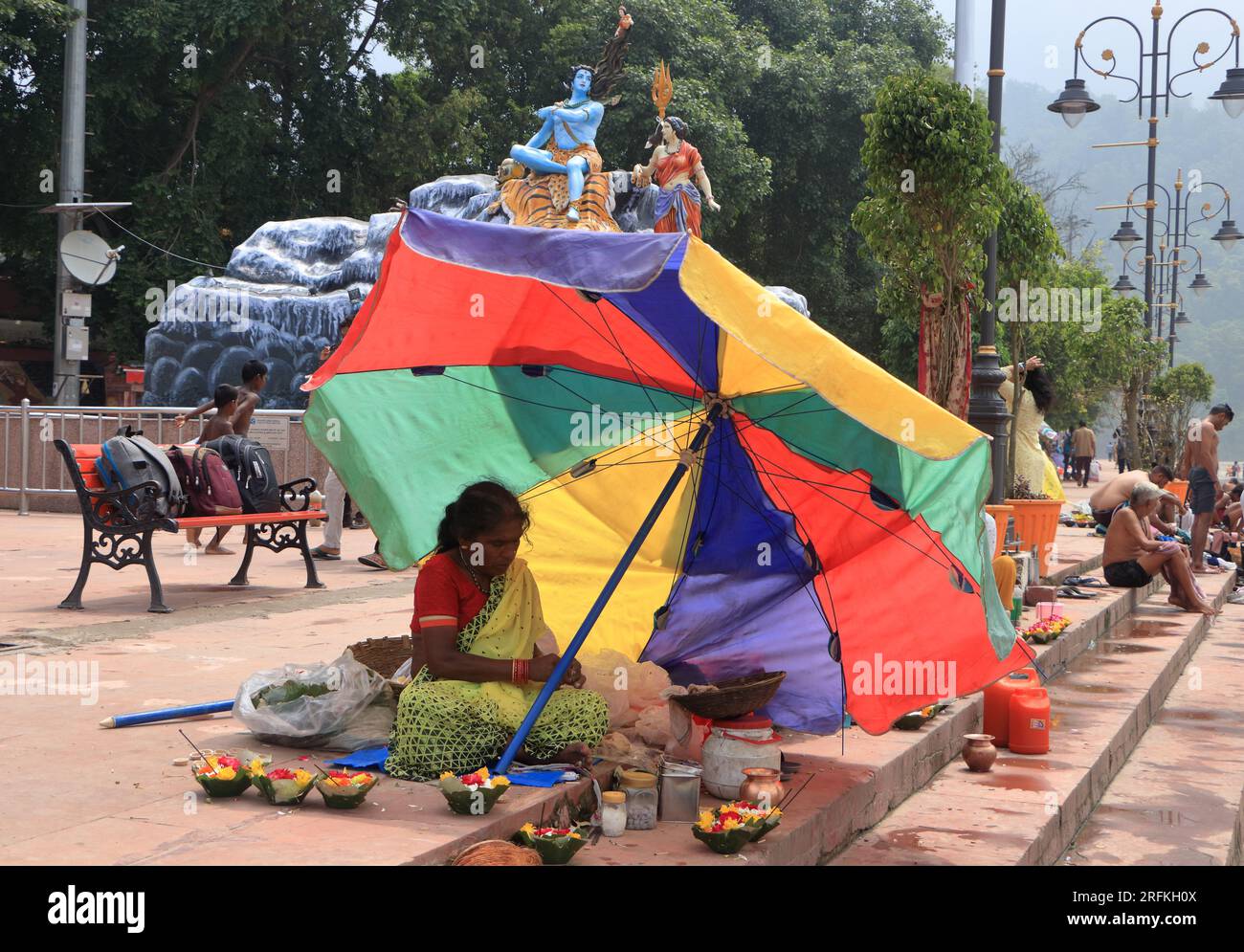 Une pauvre femme vendant des articles de puja à Triveni Ghat, Rishikesh, tenant un parapluie pour se protéger du soleil. Rishikesh. Uttarakhand. Inde. Asie. Banque D'Images