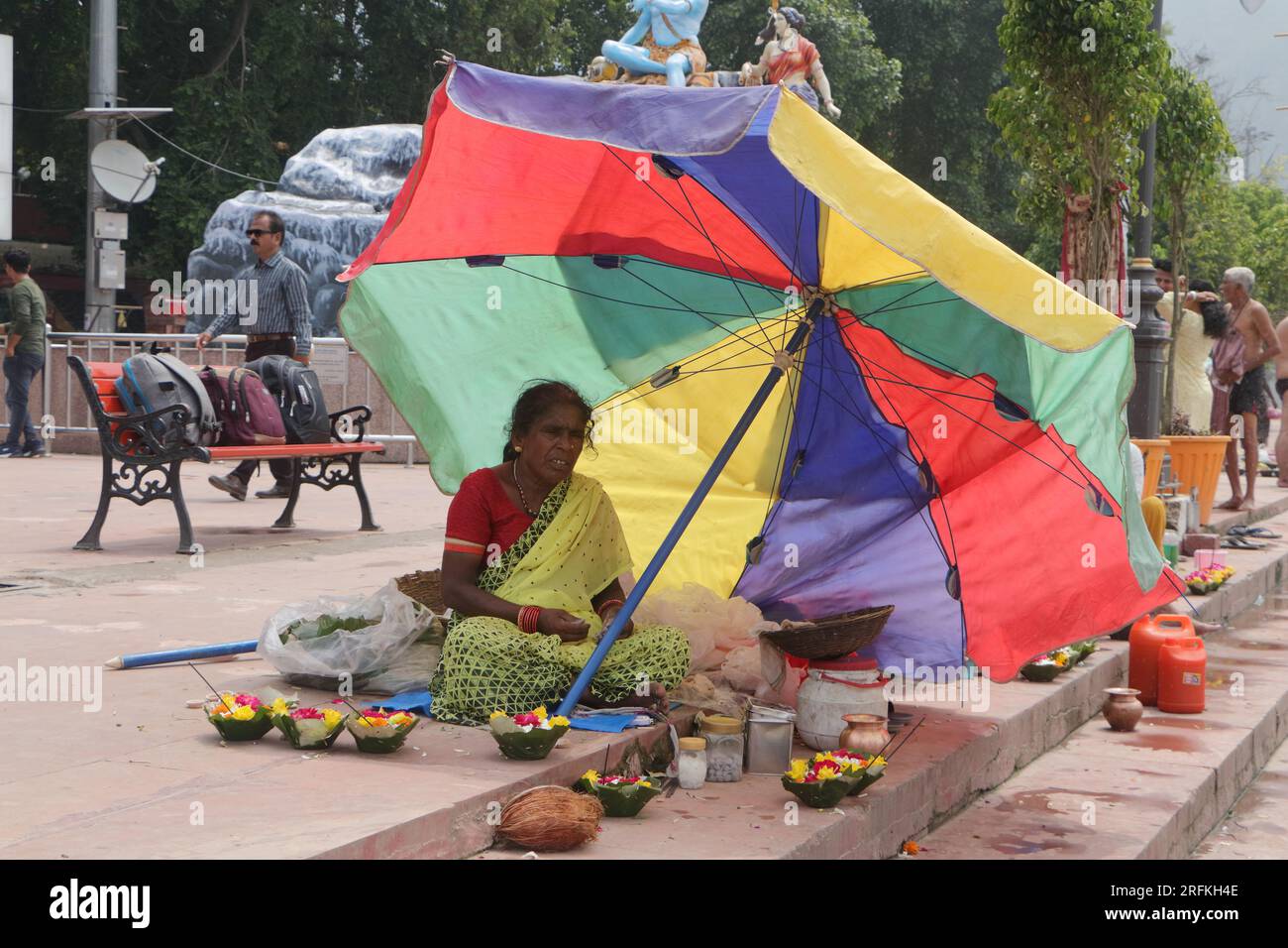 Une pauvre femme vendant des articles de puja à Triveni Ghat, Rishikesh, tenant un parapluie pour se protéger du soleil. Rishikesh. Uttarakhand. Inde. Asie. Banque D'Images