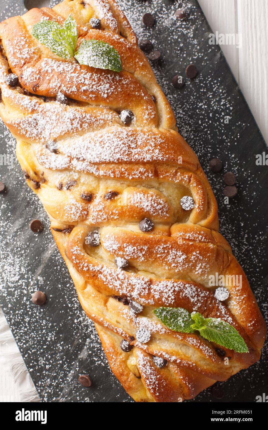 Pain sucré tressé maison doux avec chocolat et crème anglaise gros plan sur une planche d'ardoise sur la table. Vue verticale de dessus Banque D'Images