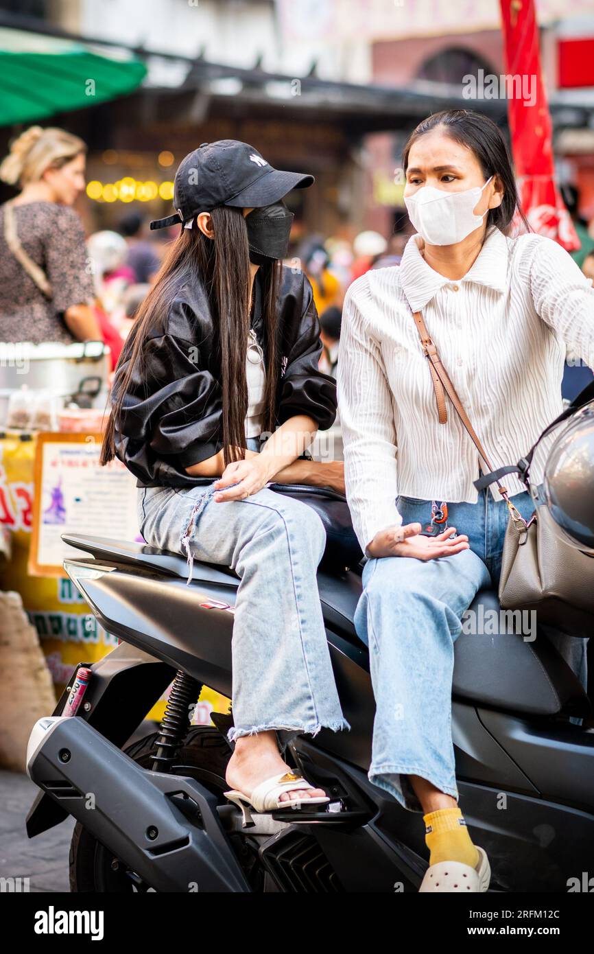 Deux filles thaïlandaises profondément dans la conversation assis sur leur cyclomoteur à Yaowarat Rd. Marché, China Town, Bangkok Thaïlande. Banque D'Images