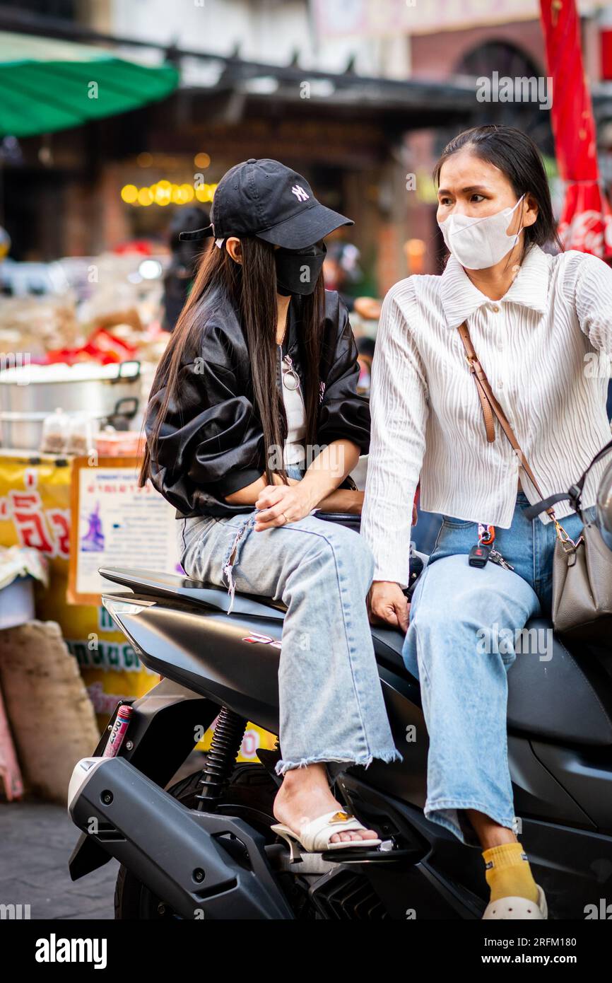 Deux filles thaïlandaises profondément dans la conversation assis sur leur cyclomoteur à Yaowarat Rd. Marché, China Town, Bangkok Thaïlande. Banque D'Images