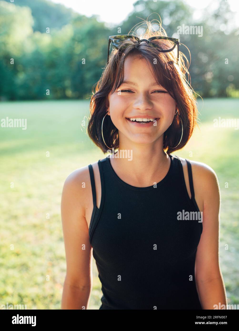 Une belle jeune adolescente souriant joyeusement à la caméra avec un chaud coucher de soleil rétro-éclairé bokeh. De belles personnes et une image de concept de mode. Banque D'Images