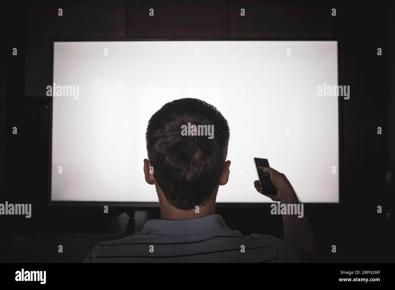Homme regardant la télévision, allumant le téléviseur à écran plat plasma, pointant la télécommande vers un écran de télévision vide sur le mur. Guy changer de chaîne à la maison, à l'arrière Banque D'Images