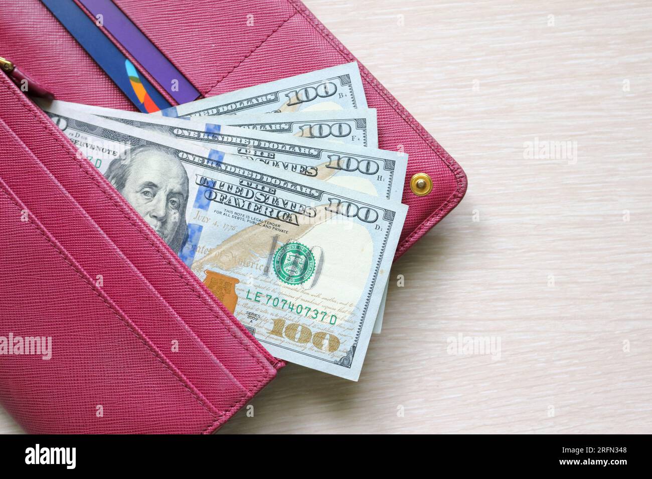 Des billets de cent dollars dans un portefeuille en cuir. Portefeuille rouge Fucsia, sac à main. Fond en bois. Billets de banque. Argent en espèces. Pile de notes. Fan de billets. USD Banque D'Images