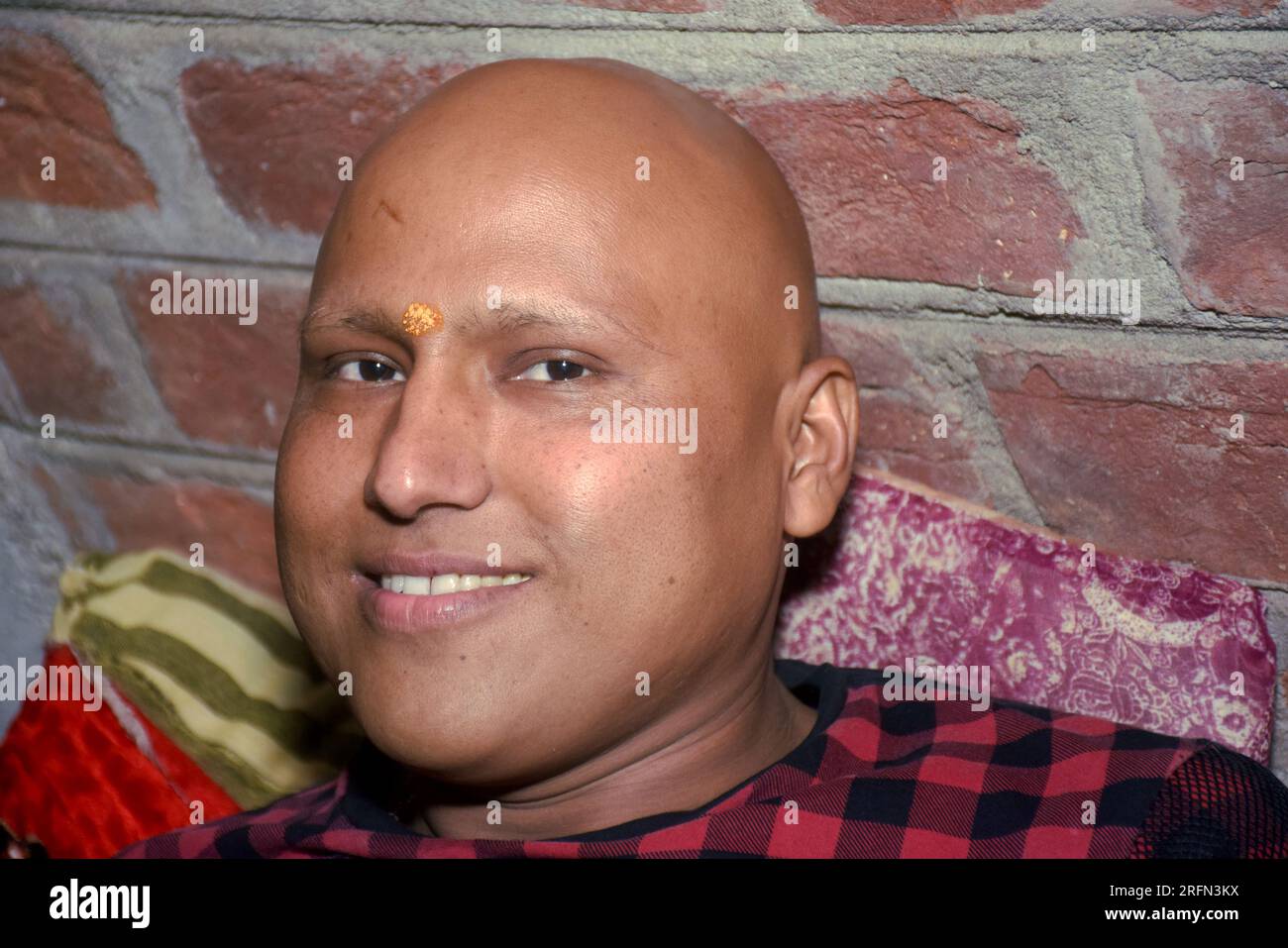 Indien chauve et rasé jeune homme propre couché souriant, mur de briques en arrière-plan. Banque D'Images