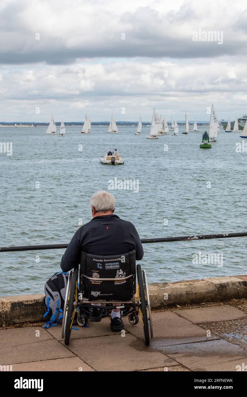 homme assis dans un fauteuil roulant au bord de la mer regardant la course de yacht à la cowes week regtta annuelle sur l'île de wight royaume-uni Banque D'Images