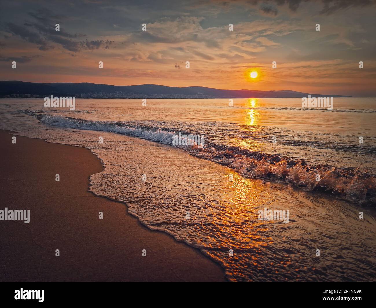 Paysage marin paisible, bord de mer silencieux le matin avec beau lever de soleil au-dessus des collines et vagues mousseuses frappant le sable. Aube à la mer, fond de voyage Banque D'Images