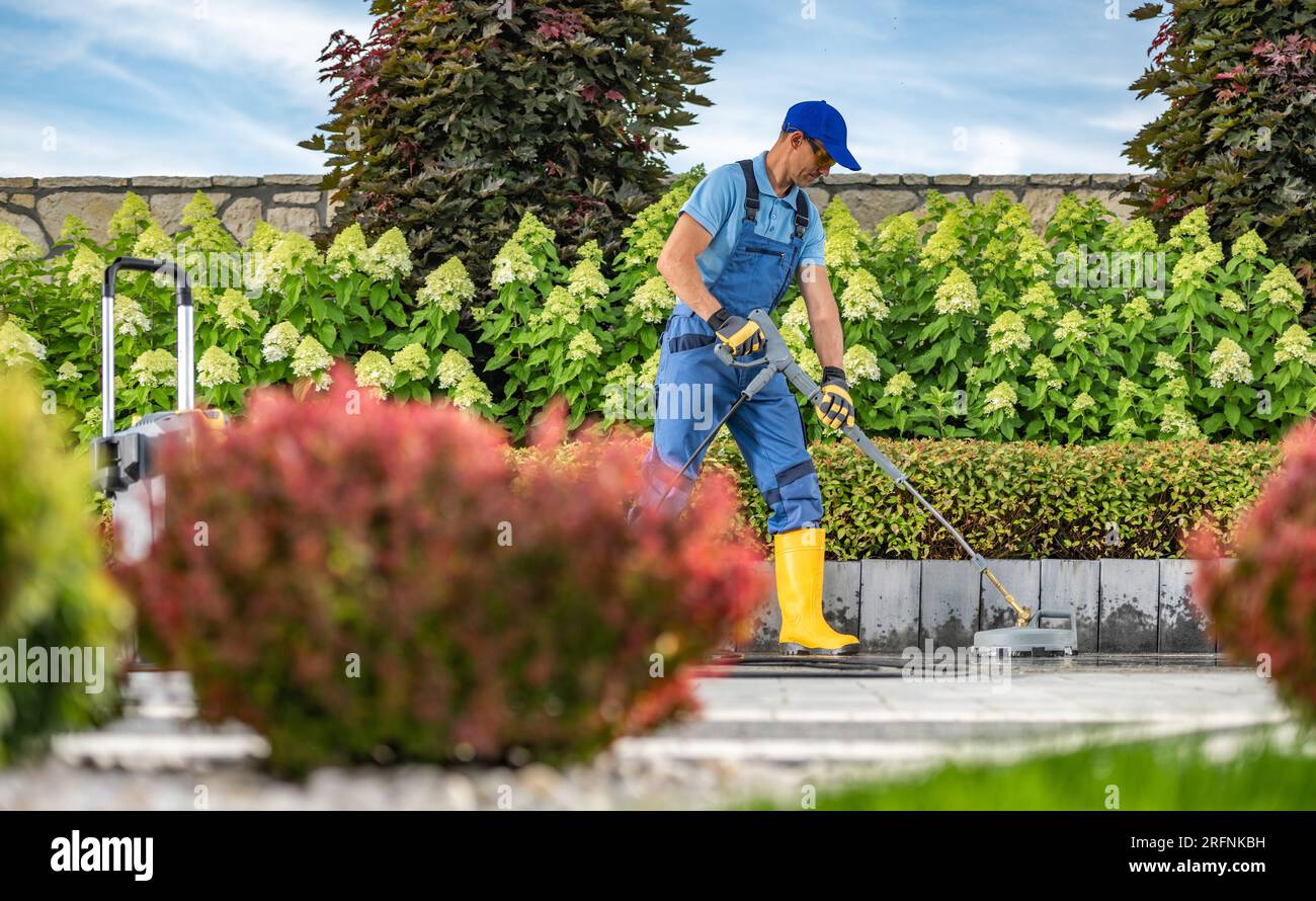 Caucasian Worker Power Washing briques en béton allée à l'aide d'un nettoyeur haute pression Banque D'Images