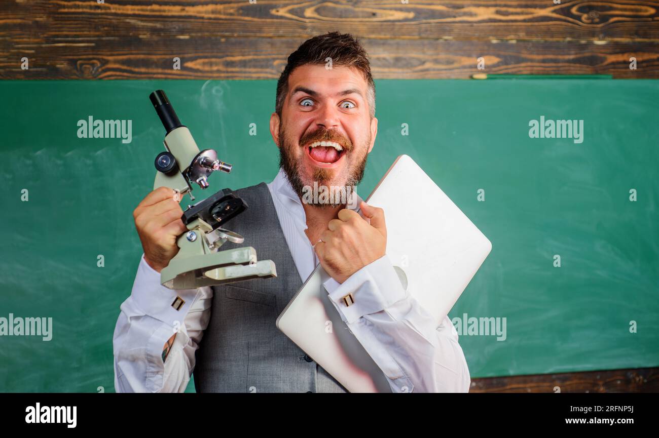 Étudiant ou professeur heureux avec ordinateur portable et microscope en classe. Homme barbu avec cahier et microscope. Cours de biologie ou de chimie. Éducation Banque D'Images