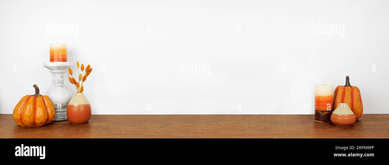 Décor d'automne sur une étagère en bois sur un fond de mur blanc. Bannière avec espace de copie. Bougies, citrouilles et vases aux couleurs d'automne. Banque D'Images
