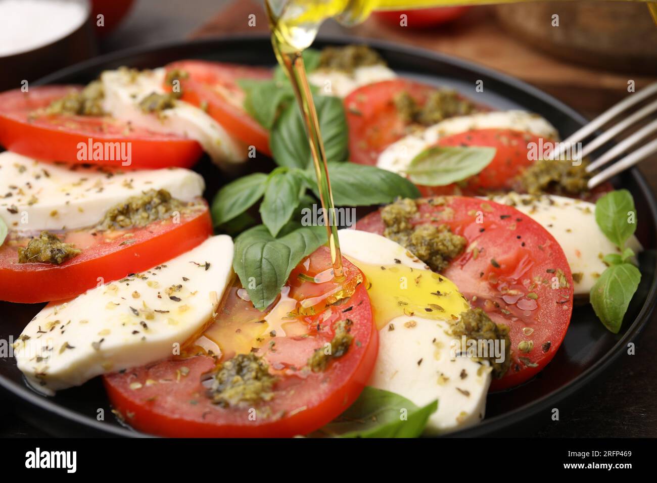 Verser l'huile d'olive sur la délicieuse salade Caprese avec sauce pesto sur la table, gros plan Banque D'Images