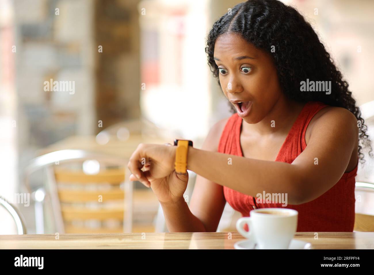 Femme noire émerveillée vérifiant smartwatch dans une terrasse de bar Banque D'Images