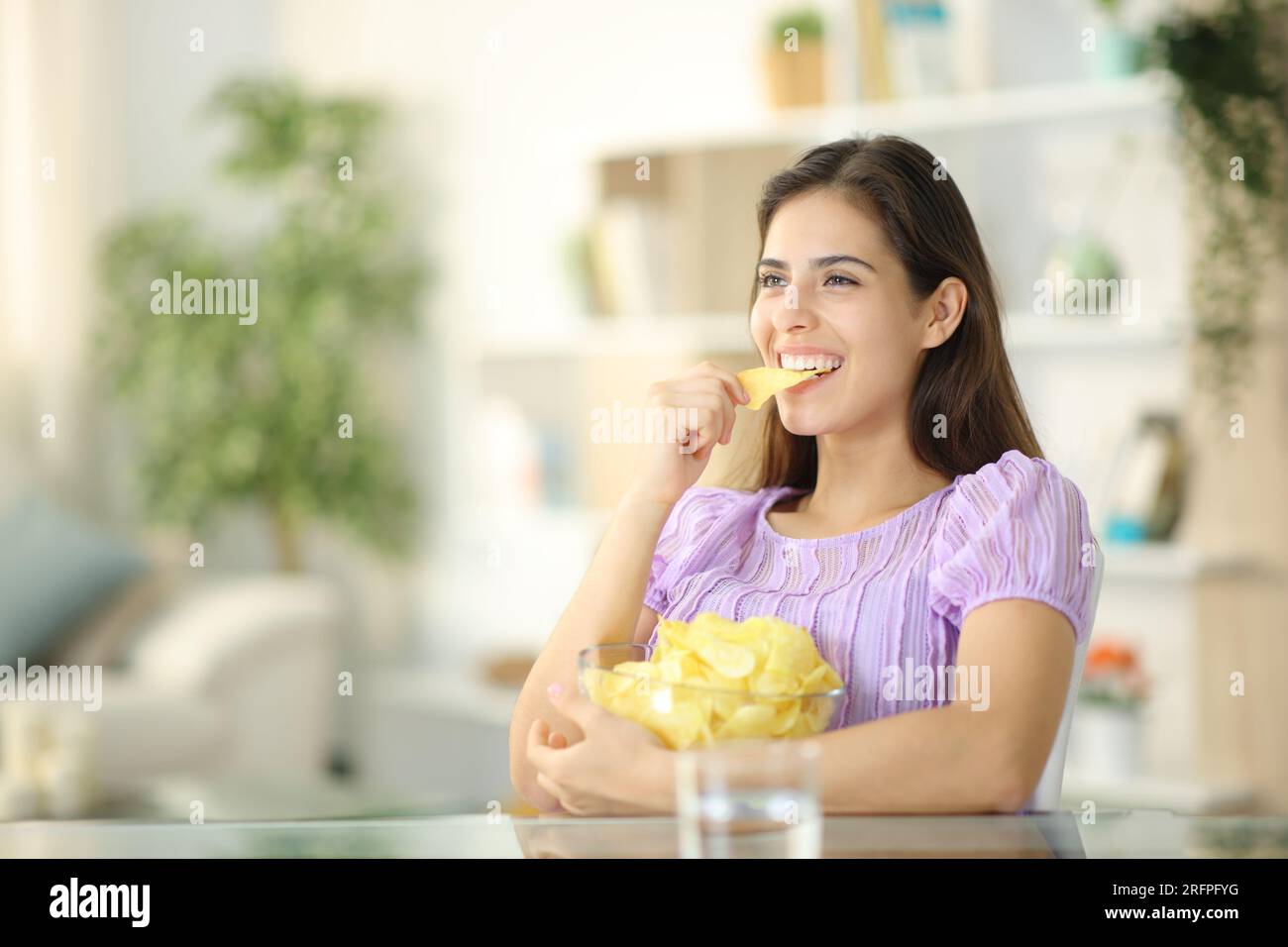 Femme heureuse mangeant des chips assis dans le salon à la maison Banque D'Images