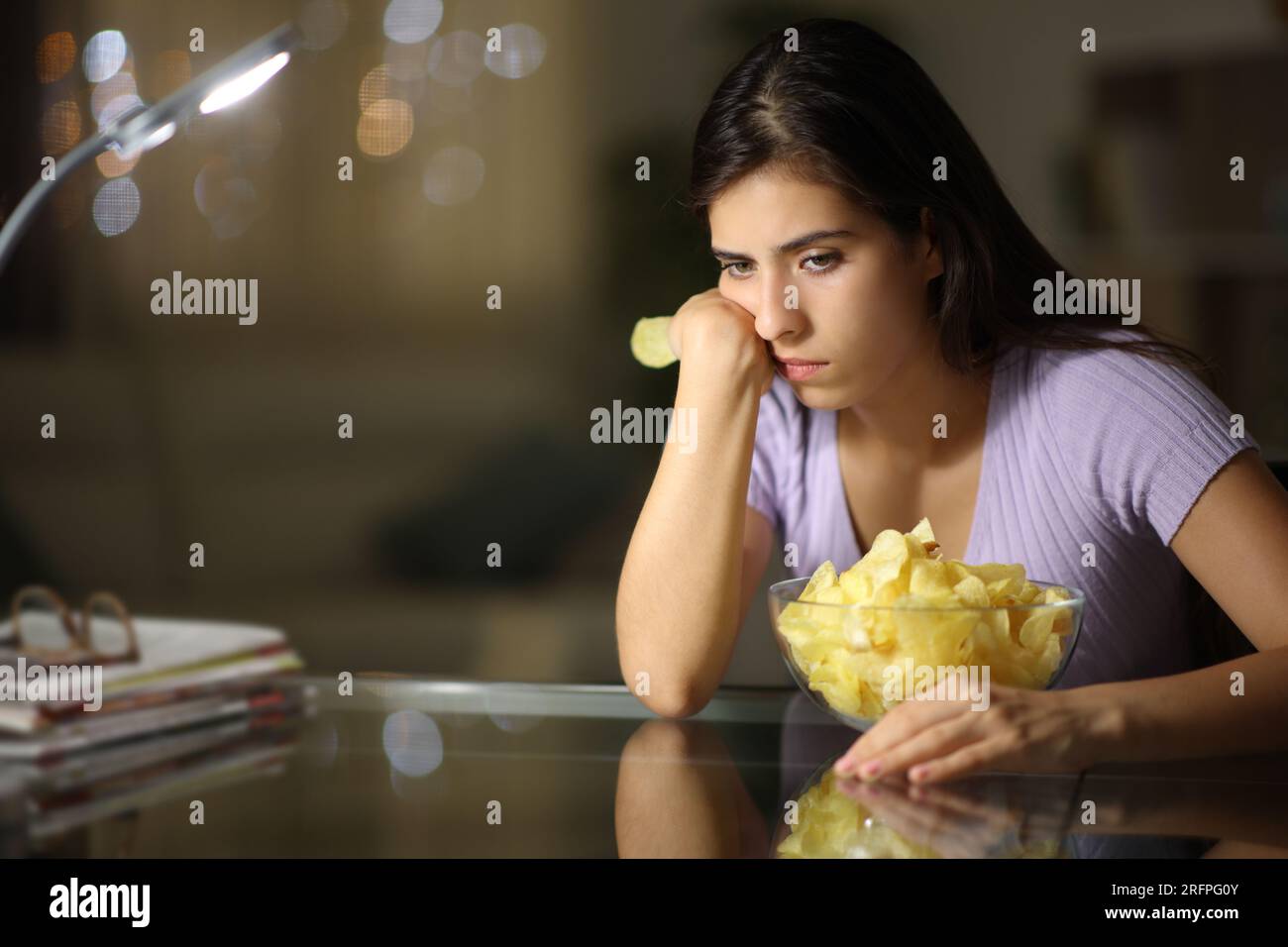 Femme triste mangeant des chips de pommes de terre se plaignant dans la nuit à la maison Banque D'Images