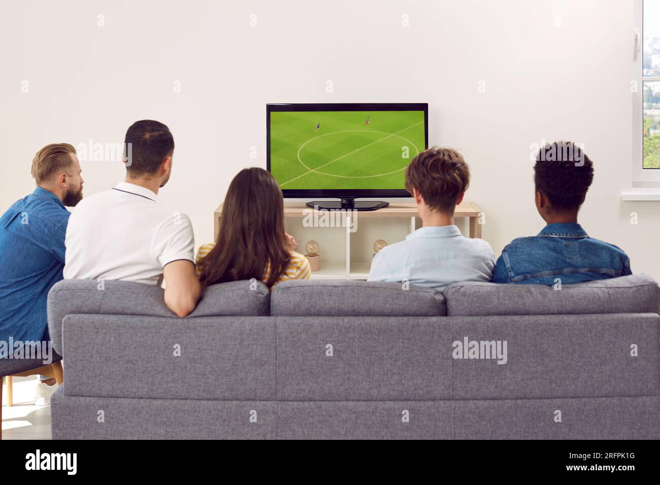 Amis multinationaux - les fans se sont rassemblés, assis sur un canapé dans une grande salle pour regarder un match de football à la télévision. Banque D'Images