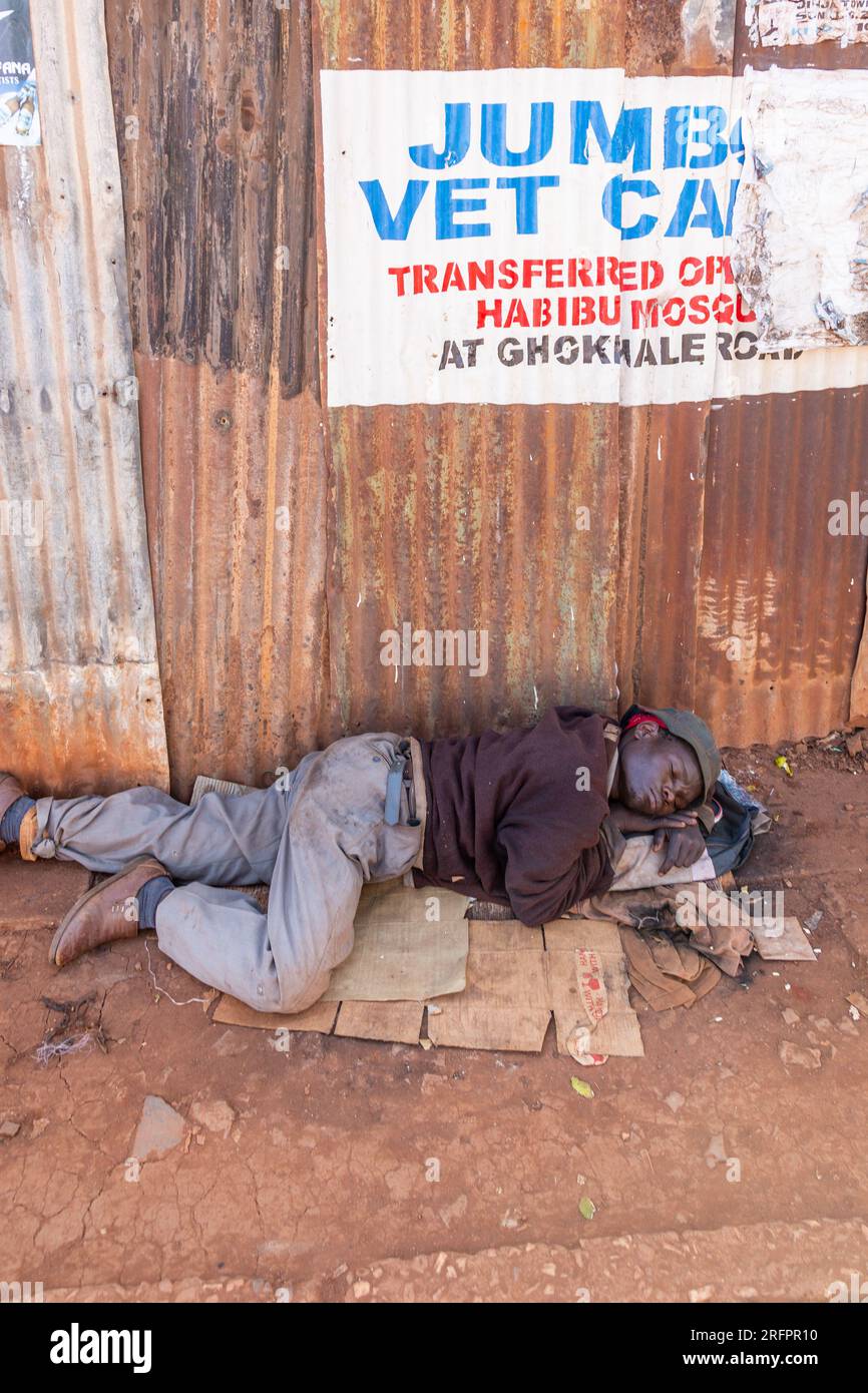 Homme faisant une sieste, allongé sur un carton dans la rue. Jinja, Ouganda. Banque D'Images