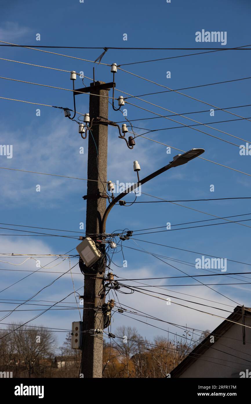 Fils électriques accrochés à un poteau avec une lampe d'éclairage photographiée d'en dessous sur un fond de ciel bleu. Banque D'Images