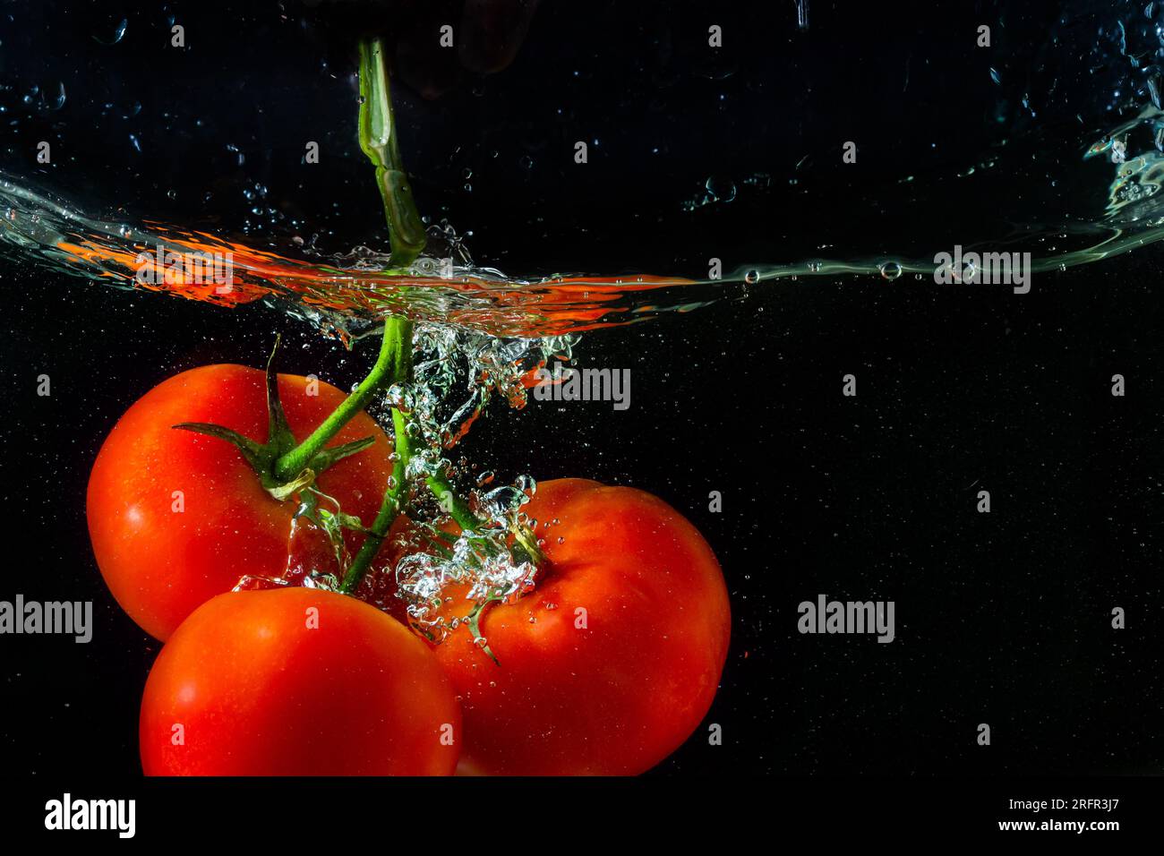 Tomate rouge fraîche tombant dans l'eau avec des éclaboussures d'eau et des bulles d'air isolées sur fond noir. Banque D'Images