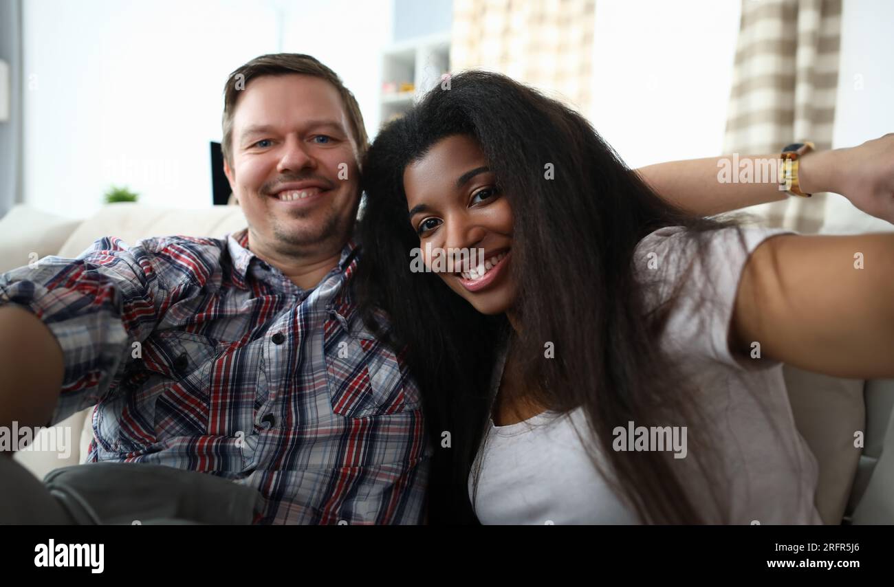 Portrait de joyeux couple de race mixte prenant un selfie heureux sur le canapé à l'intérieur. Banque D'Images