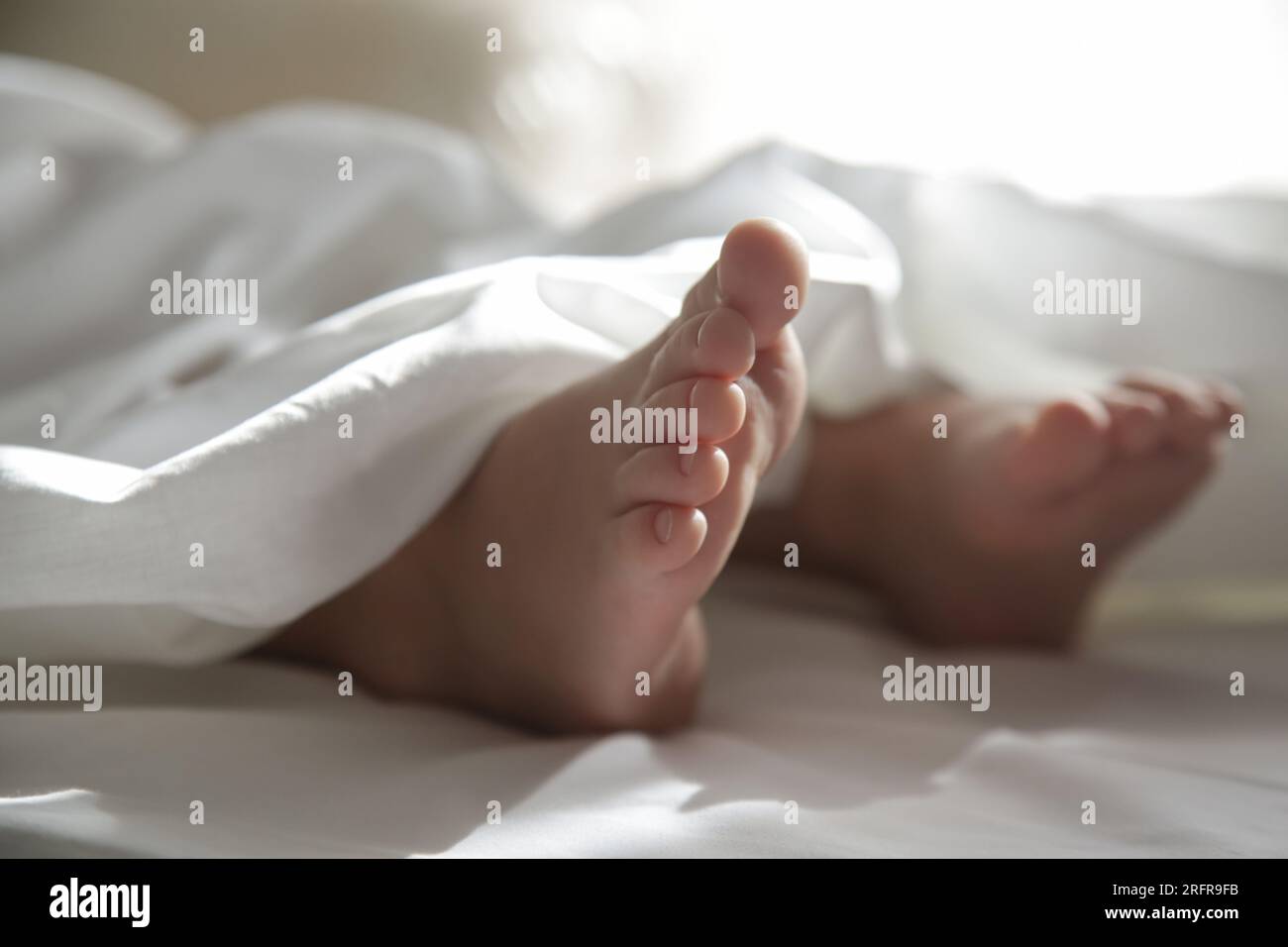 Pieds d'enfant sous la couverture blanche sous la lumière douce du matin Banque D'Images