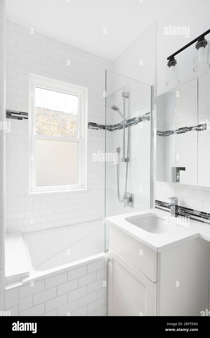 Une salle de bains avec murs de carreaux de métro blancs, armoire et comptoir avec une fenêtre dans la douche. Banque D'Images