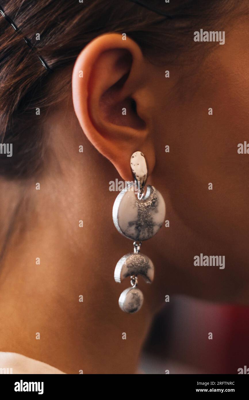 Boucle d'oreille blanche argentée décorative accrochée dans l'oreille d'une femme. Détails de mode et accessoires Banque D'Images