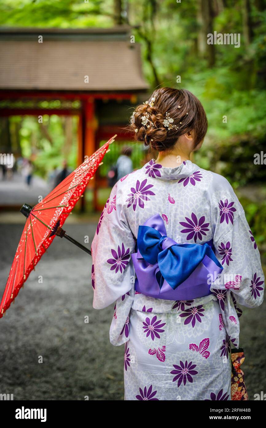 Vue arrière d'une femme portant un kimono d'été japonais yukata et tenant un parapluie japonais traditionnel en papier d'huile dans la porte de la forêt naturelle du sanctuaire Kifune, Banque D'Images