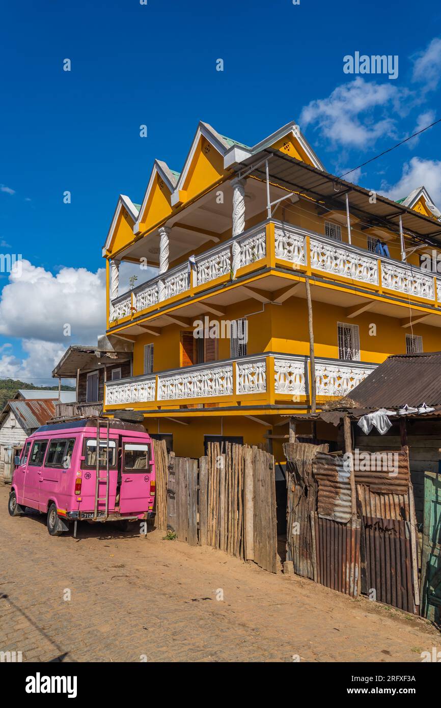 Andasibe, Madagascar - 26 mai 2023 : une voiture rose de transport public devant une maison jaune à Andasibe Banque D'Images