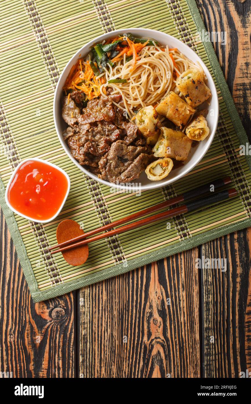 Salade vietnamienne de bœuf et sauce soja, avec des rouleaux de printemps croustillants et des nouilles de riz, des herbes fraîches, des légumes en gros plan sur la table. Vue verticale de dessus Banque D'Images