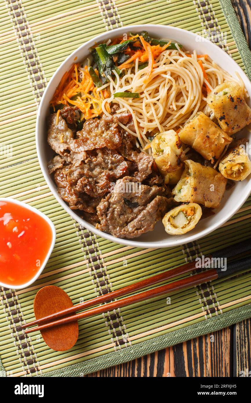 Salade vietnamienne faite avec du bœuf, des vermicelles de riz, des légumes et des rouleaux de printemps frits gros plan sur la table. Vue verticale de dessus Banque D'Images