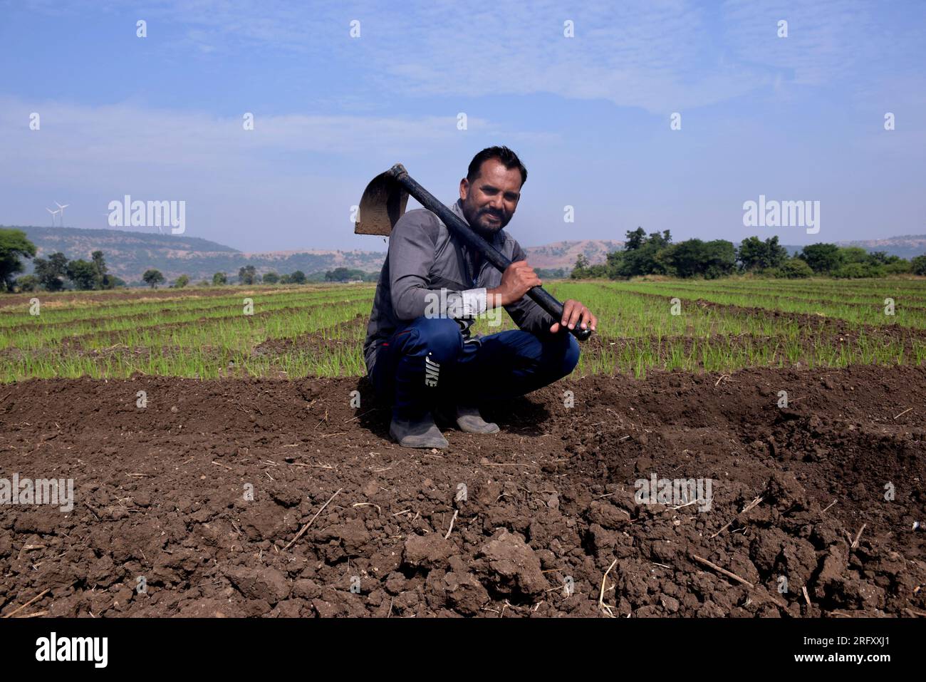 Fermier indien assis dans le champ avec une pelle, lent après avoir travaillé dans le champ, la verdure et le fond du ciel Banque D'Images