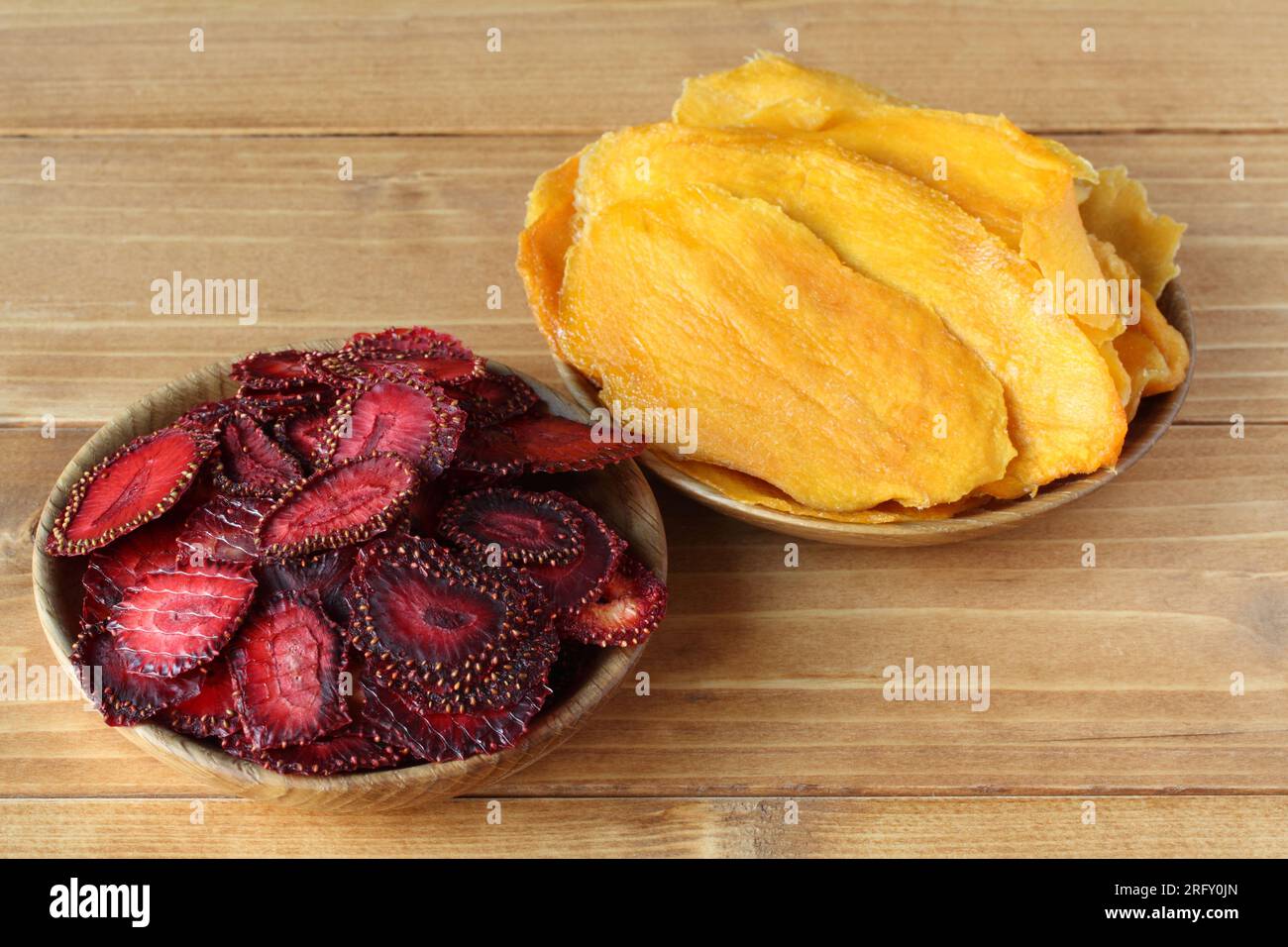 Des morceaux de fraises séchés et des morceaux de mangue séchés se trouvent sur des soucoupes en bois qui se tiennent sur une table en bois. Vue de dessus Banque D'Images