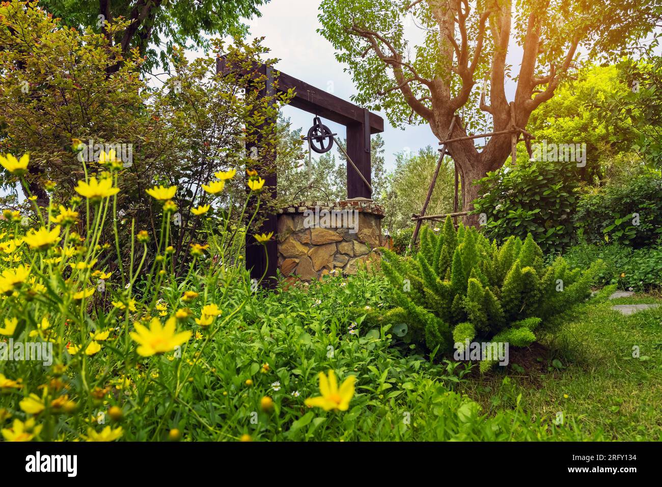Magnifique bien artesian fait de pierres et poulie de roue avec seau en métal et corde dans une atmosphère paisible de jardin. Puits rétro en pierre dans la zone rurale Banque D'Images