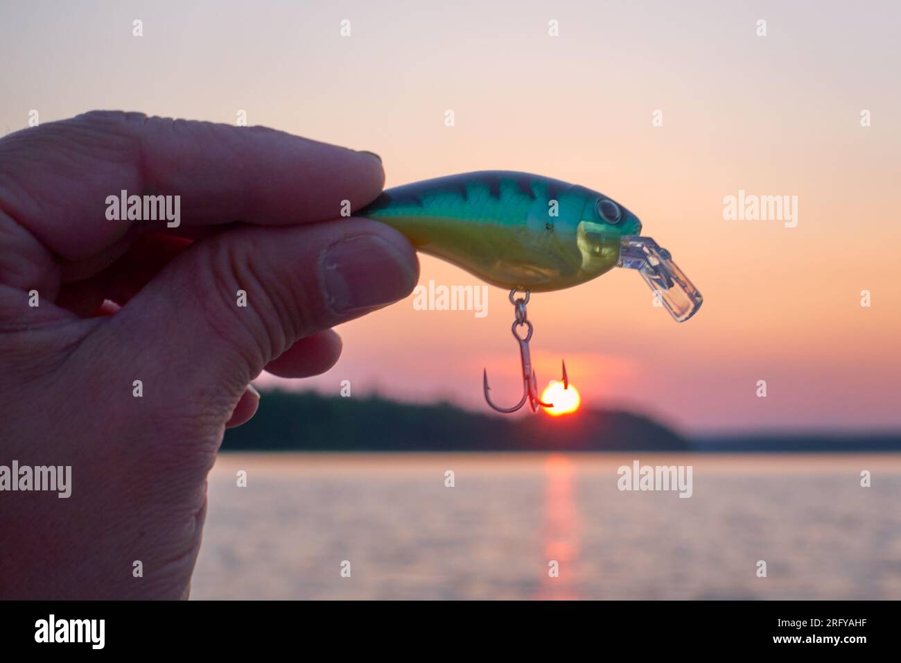 Pêcheur mâle tenant un petit leurre wobbler qui accrochait un soleil couchant sur un lac dans l'ouest de la Finlande. Banque D'Images