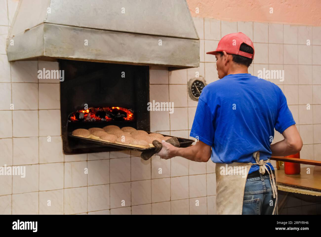 Dans une boulangerie mexicaine traditionnelle, le dos d'un boulanger est tourné alors qu'il récupère des conchas au chocolat fraîchement cuit dans le four. Son visage reste invisible, emph Banque D'Images