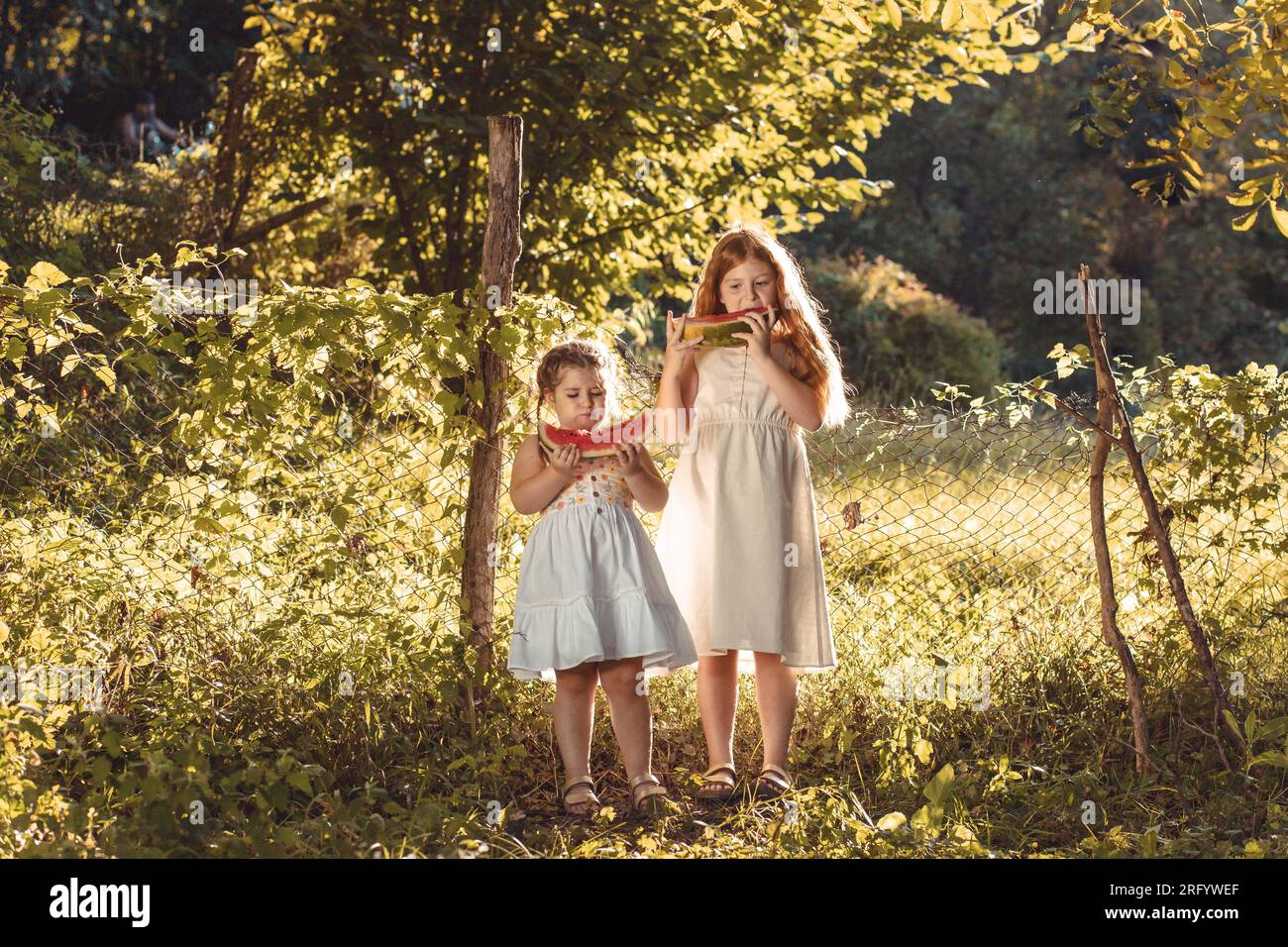 Deux petites filles, sœurs dehors en robes blanches, mangeant de la pastèque. Espace de copie Banque D'Images