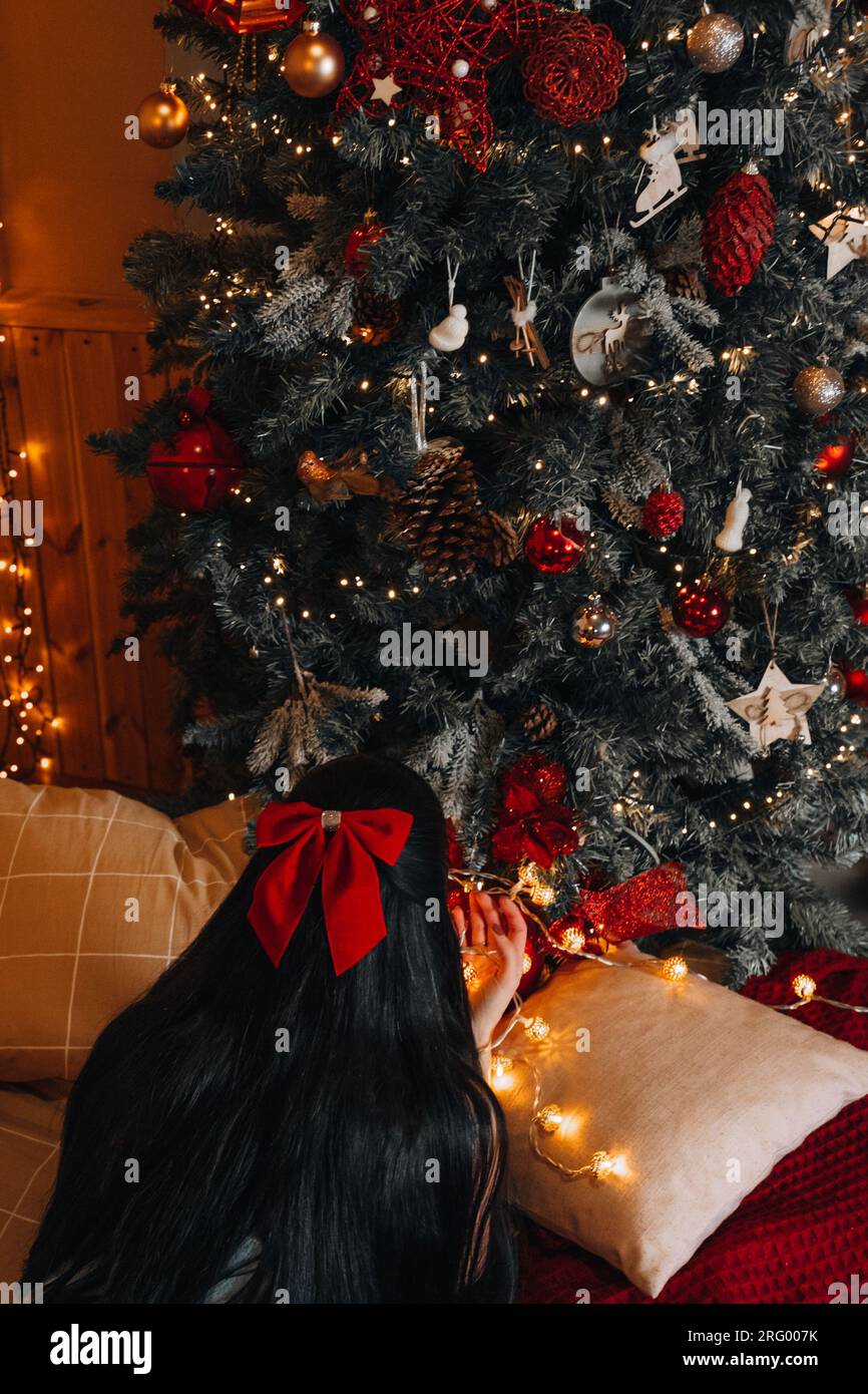 Une femme brune avec un arc rouge en cheveux noirs couchée près de l'arbre de Noël avec des décorations festives. Nouvel an et Joyeux Noël de vacances d'hiver déco Banque D'Images