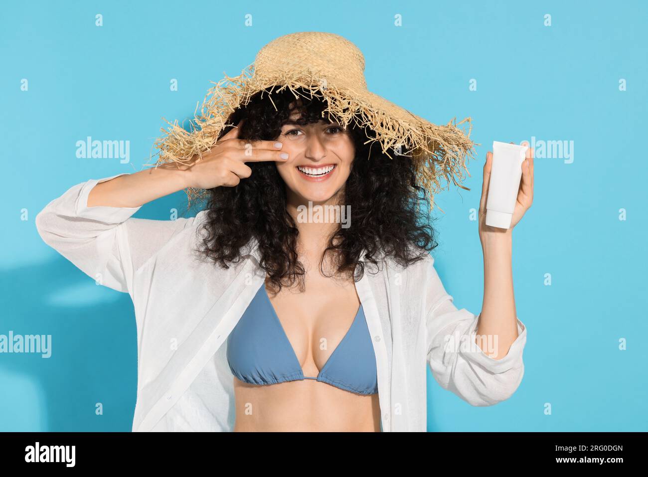 Belle jeune femme dans le chapeau de paille avec tube de crème solaire sur fond bleu clair Banque D'Images