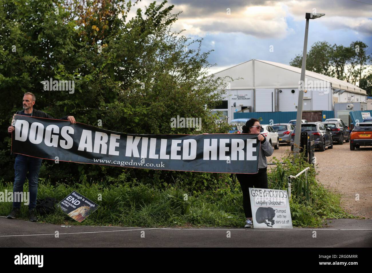 Henlow, Royaume-Uni. 06 août 2023. Les manifestants brandissent une banderole à l'extérieur du stade pour chiens disant "les chiens sont tués ici" pendant la manifestation. Les militants des droits des animaux manifestent devant la piste de courses de chiens Henlow. Ils visent à souligner la cruauté associée aux courses de chiens. En 2021, il y a eu 4422 blessés et 120 morts sur les pistes de courses de lévriers enregistrées au Royaume-Uni. Crédit : SOPA Images Limited/Alamy Live News Banque D'Images