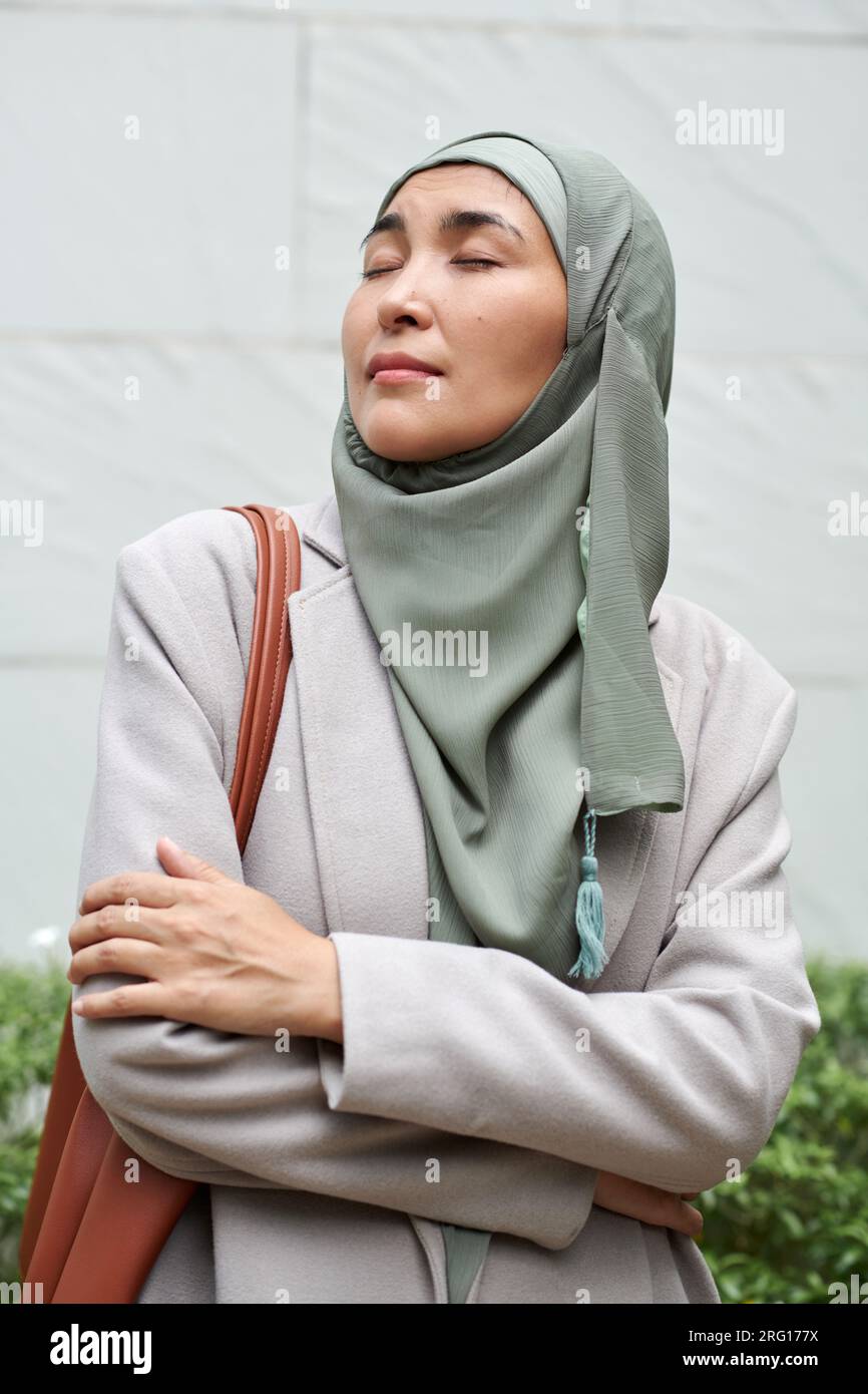 Portrait d'une femme d'affaires musulmane dans le hijab debout à l'extérieur, croisant les bras et profitant de l'air frais Banque D'Images