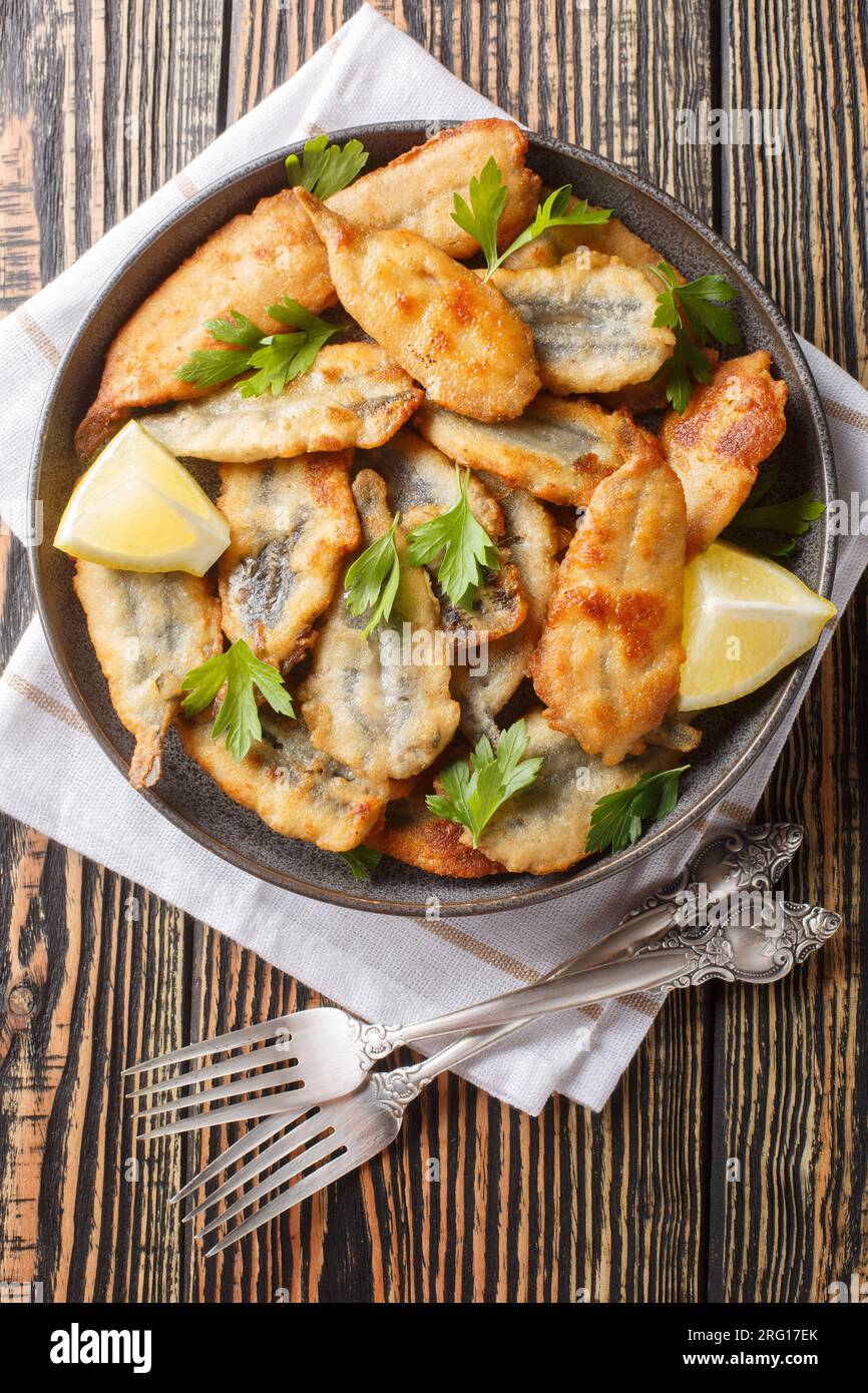 Anchois frits servis avec citron et herbes en gros plan sur une assiette sur la table. Vue verticale de dessus Banque D'Images