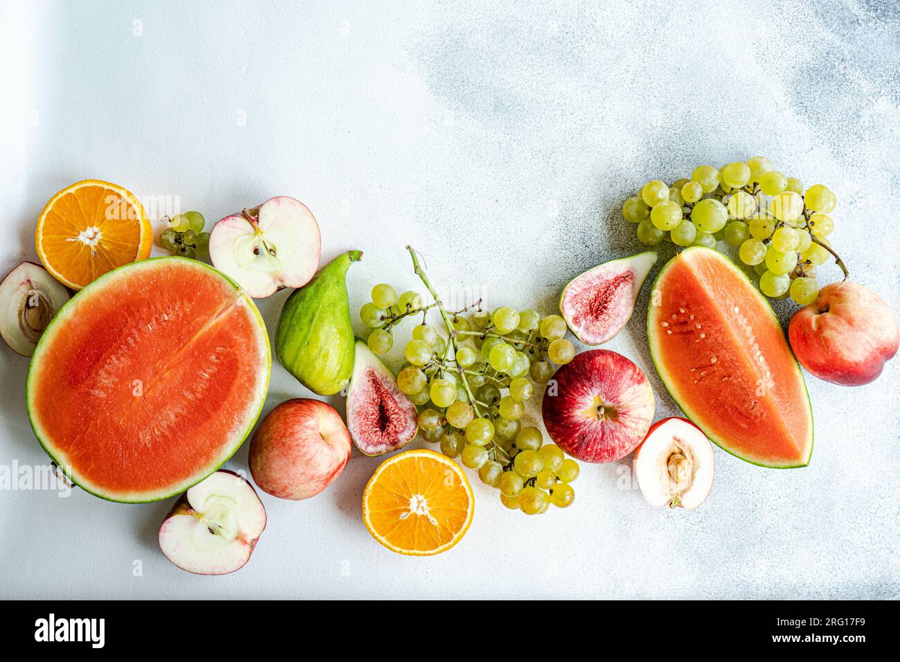 Vue de dessus du cadre de fruits de saison composé de pastèque, raisins, orange, poire et pomme placé sur une surface blanche Banque D'Images