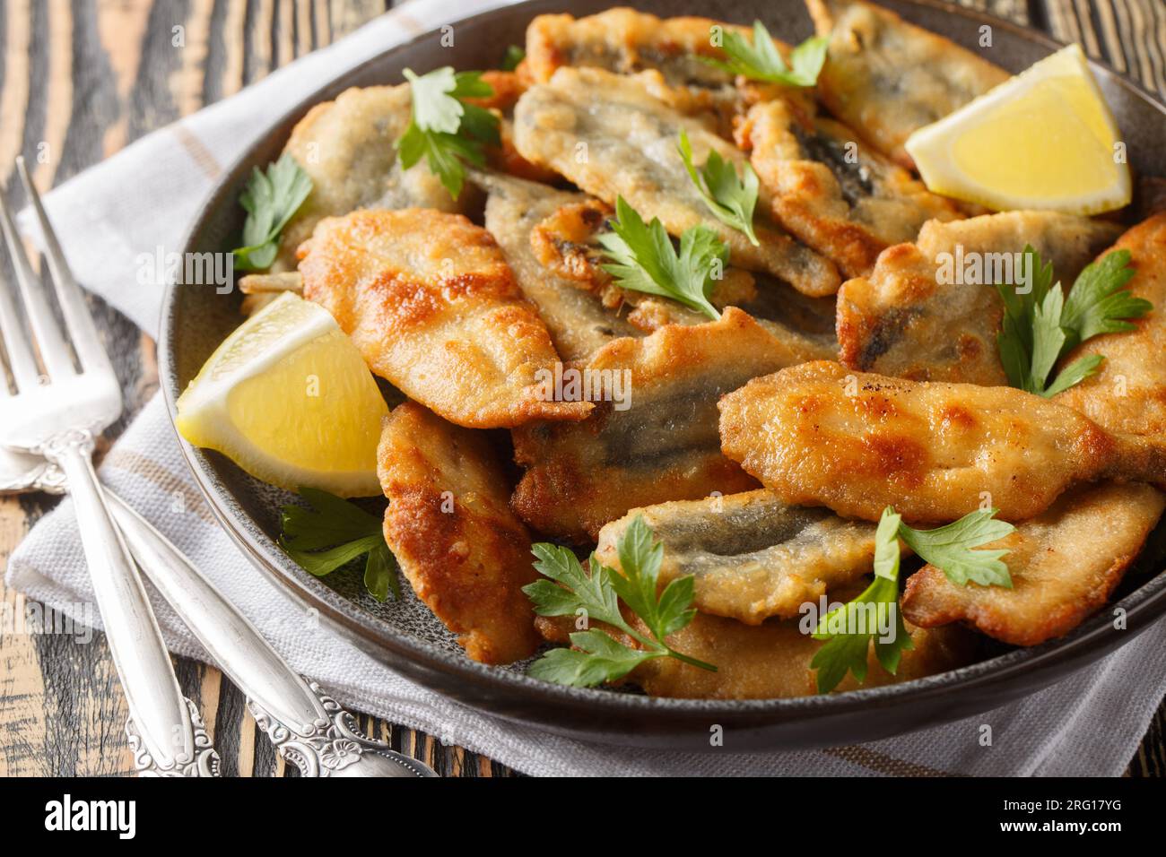 Filets d'anchois panés frits servis avec du citron et des herbes en gros plan sur une assiette sur la table. Horizontal Banque D'Images