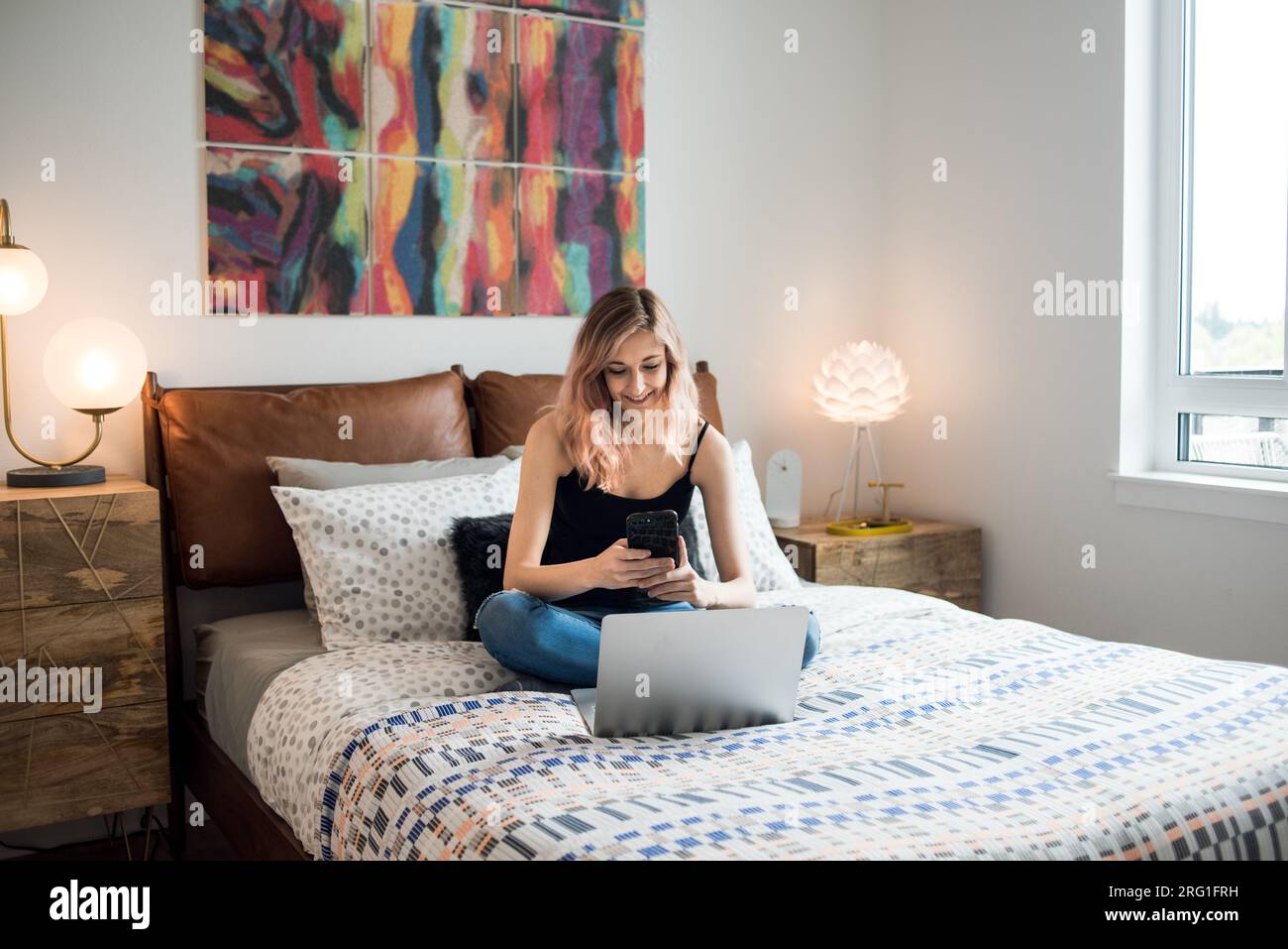 Femme assise sur le lit et souriant au téléphone Banque D'Images