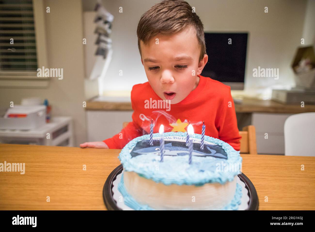 un garçon de six ans souffle des bougies sur son gâteau aux requins Banque D'Images